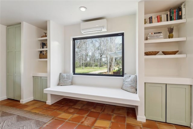 living area featuring built in features, a wall mounted air conditioner, and baseboards