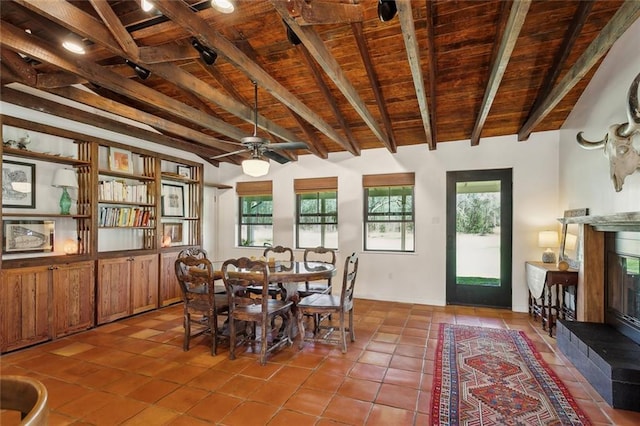 tiled dining room with a glass covered fireplace, wooden ceiling, a healthy amount of sunlight, and beam ceiling