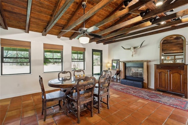 dining space with a ceiling fan, vaulted ceiling with beams, a glass covered fireplace, wooden ceiling, and tile patterned floors