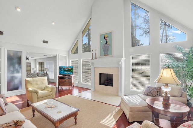 living room with visible vents, a fireplace with flush hearth, high vaulted ceiling, and wood finished floors