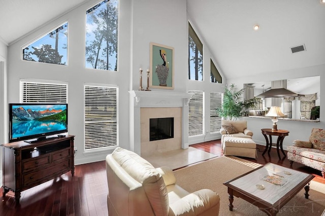 living area featuring wood finished floors, baseboards, visible vents, high vaulted ceiling, and a fireplace with flush hearth