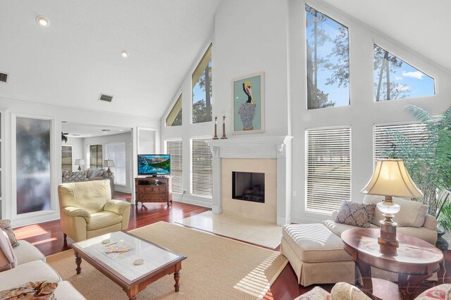 living room featuring visible vents, baseboards, a fireplace with flush hearth, wood finished floors, and high vaulted ceiling