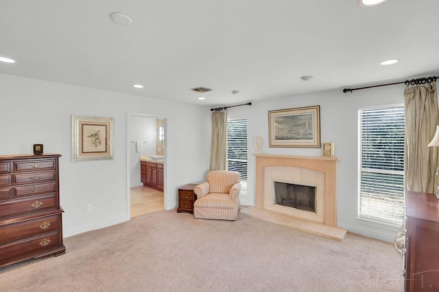 living area featuring a tiled fireplace, a healthy amount of sunlight, visible vents, and light carpet