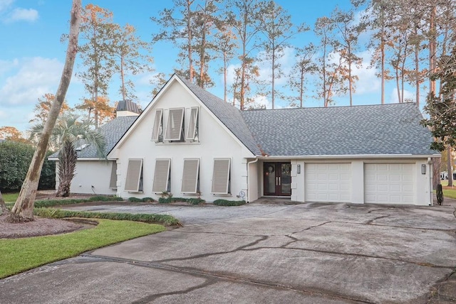 view of front of home with stucco siding, an attached garage, concrete driveway, and roof with shingles