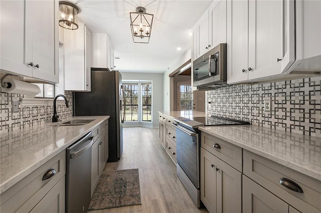 kitchen with tasteful backsplash, light stone counters, light wood-style flooring, appliances with stainless steel finishes, and a sink