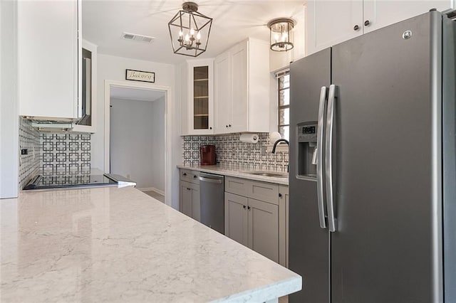 kitchen with visible vents, a sink, stainless steel appliances, white cabinets, and glass insert cabinets