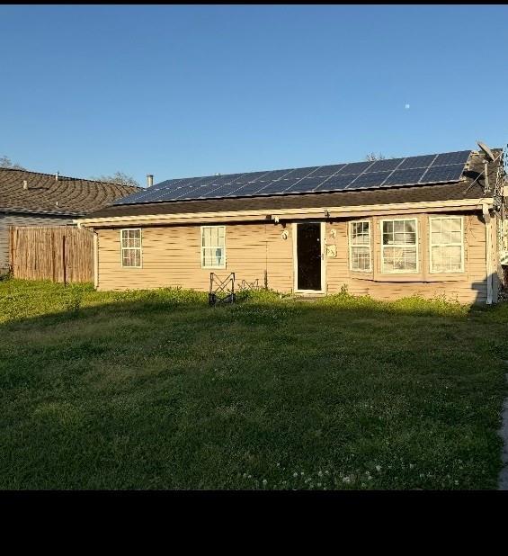 back of house with roof mounted solar panels, a yard, and fence