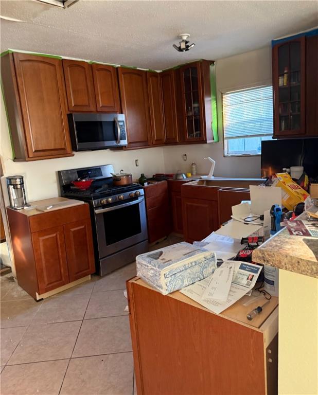 kitchen featuring a textured ceiling, appliances with stainless steel finishes, light countertops, light tile patterned floors, and glass insert cabinets