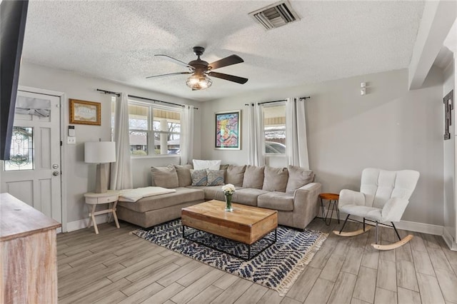 living area with visible vents, a textured ceiling, light wood-style floors, baseboards, and ceiling fan