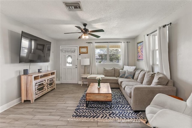 living area featuring baseboards, visible vents, wood finish floors, ceiling fan, and a textured ceiling