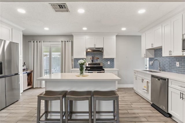 kitchen with visible vents, a breakfast bar, a sink, under cabinet range hood, and stainless steel appliances