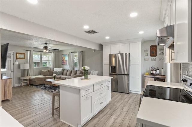 kitchen with electric range, wall chimney range hood, stainless steel fridge, light countertops, and wood tiled floor