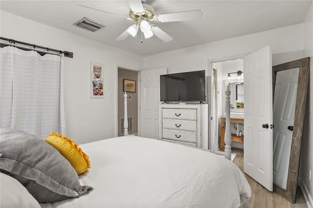 bedroom featuring connected bathroom, visible vents, light wood finished floors, and a textured ceiling