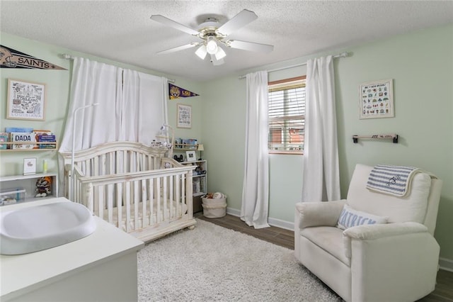 bedroom with baseboards, ceiling fan, wood finished floors, a textured ceiling, and a nursery area