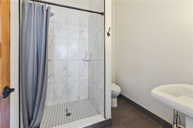 full bathroom featuring toilet, a sink, wood finished floors, a shower stall, and baseboards