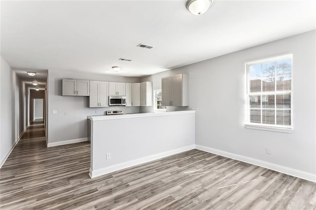 kitchen featuring stainless steel microwave, baseboards, visible vents, and wood finished floors