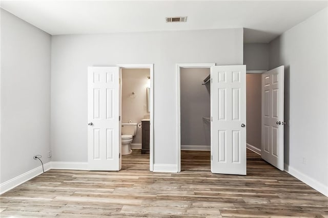 unfurnished bedroom featuring visible vents, ensuite bath, a walk in closet, and wood finished floors