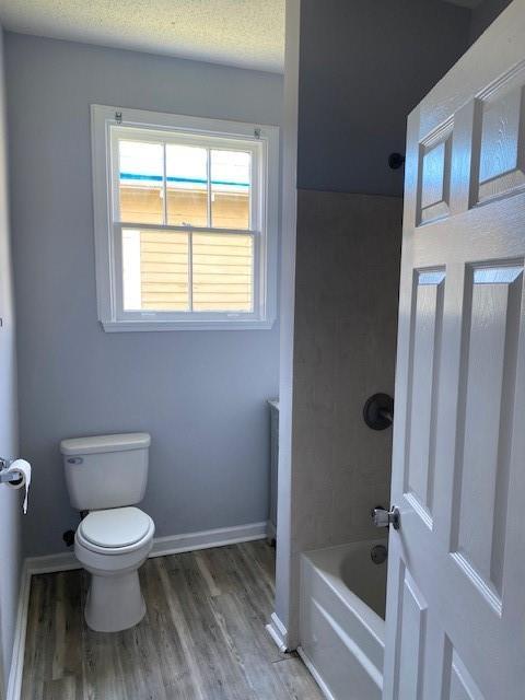 bathroom featuring toilet, shower / tub combination, baseboards, and wood finished floors