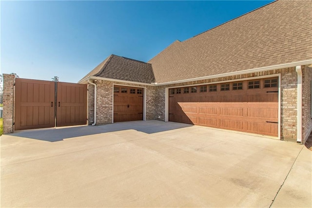 exterior space featuring concrete driveway, brick siding, a garage, and roof with shingles