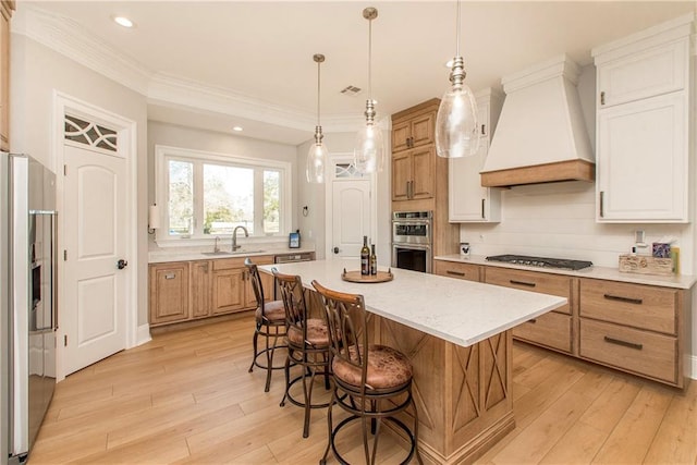 kitchen featuring light wood finished floors, a sink, stainless steel appliances, and premium range hood