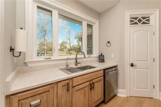 kitchen featuring light stone counters, brown cabinets, a sink, stainless steel dishwasher, and light wood-type flooring