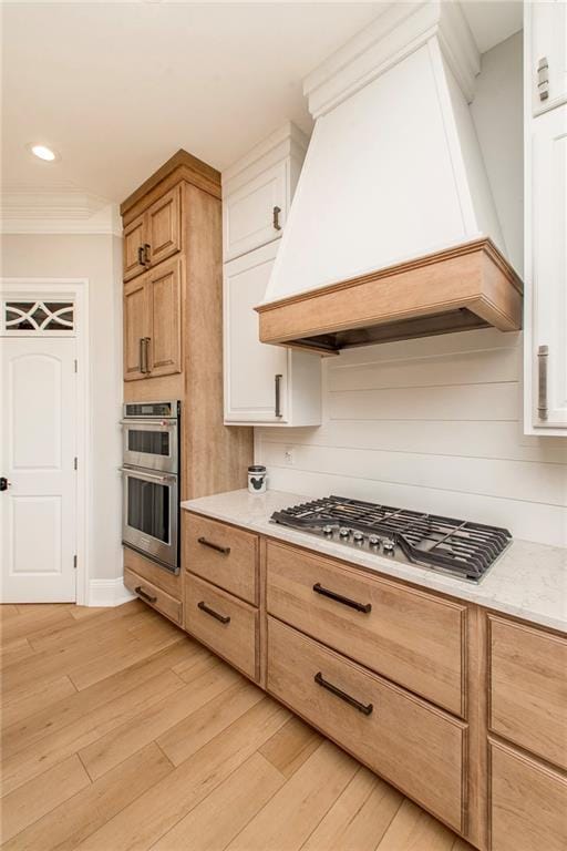 kitchen with premium range hood, stainless steel appliances, light wood-style floors, crown molding, and light countertops