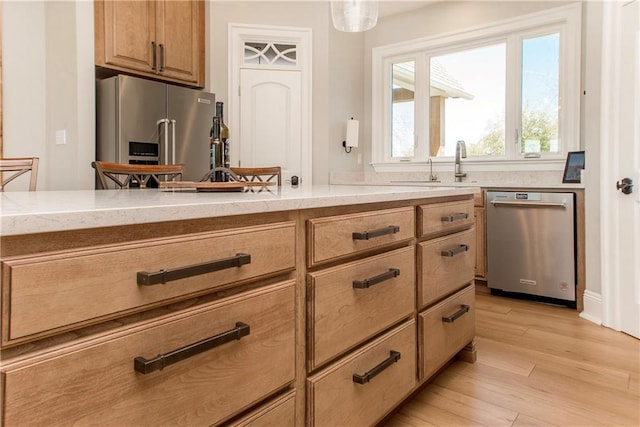 kitchen with light wood-type flooring, brown cabinets, decorative light fixtures, a sink, and stainless steel appliances