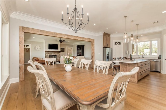 dining room with visible vents, light wood-style flooring, a fireplace, and ceiling fan with notable chandelier