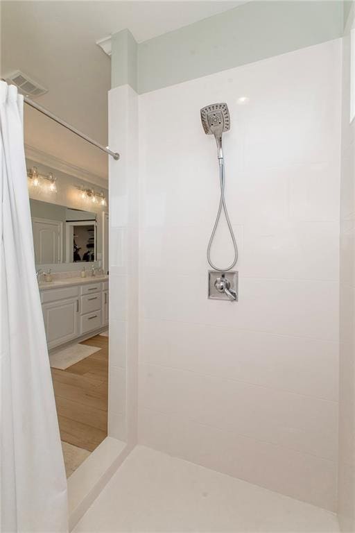 full bathroom with visible vents, tiled shower, vanity, and wood finished floors