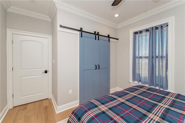 bedroom featuring light wood-style flooring, baseboards, a barn door, and ornamental molding