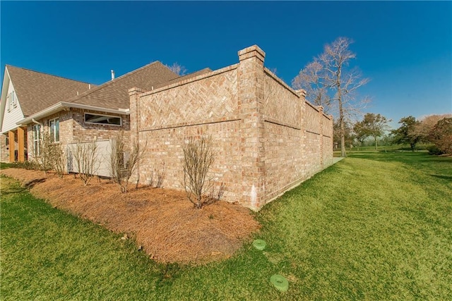 view of side of property with brick siding, a yard, and roof with shingles