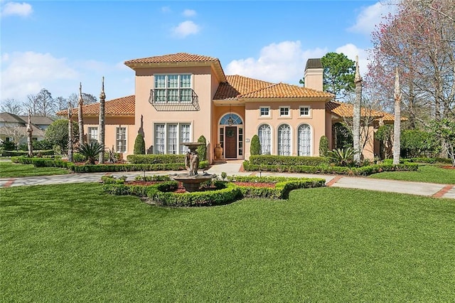 mediterranean / spanish home featuring a tile roof, stucco siding, a front lawn, and curved driveway