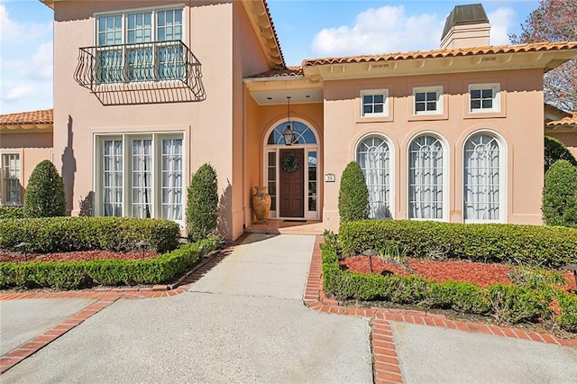 property entrance featuring a tile roof, a chimney, and stucco siding