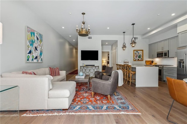 living room featuring light wood-type flooring, visible vents, a chandelier, and recessed lighting