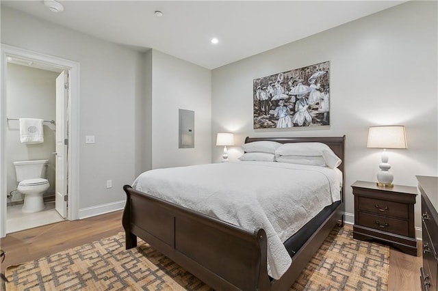 bedroom featuring wood finished floors, baseboards, electric panel, recessed lighting, and connected bathroom