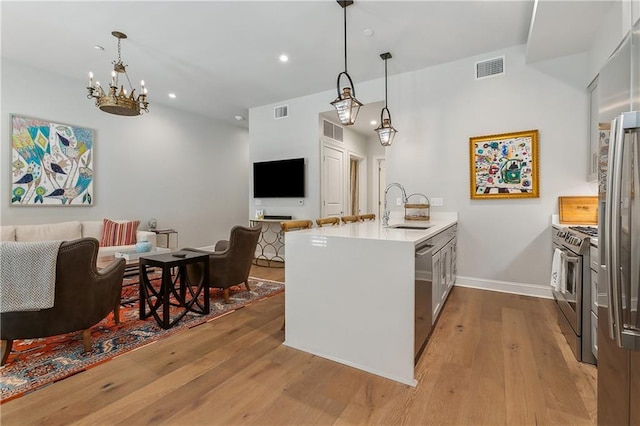 kitchen with wood finished floors, a sink, a peninsula, open floor plan, and stainless steel appliances
