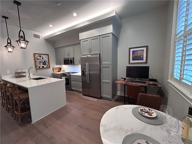 kitchen featuring visible vents, wood finished floors, gray cabinets, a sink, and stainless steel appliances