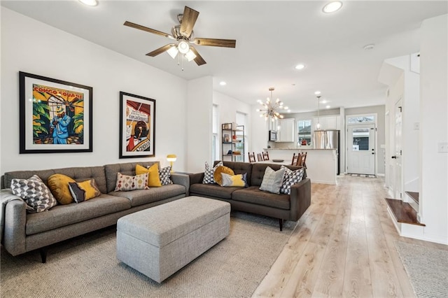 living room with recessed lighting, light wood-style flooring, ceiling fan with notable chandelier, and baseboards