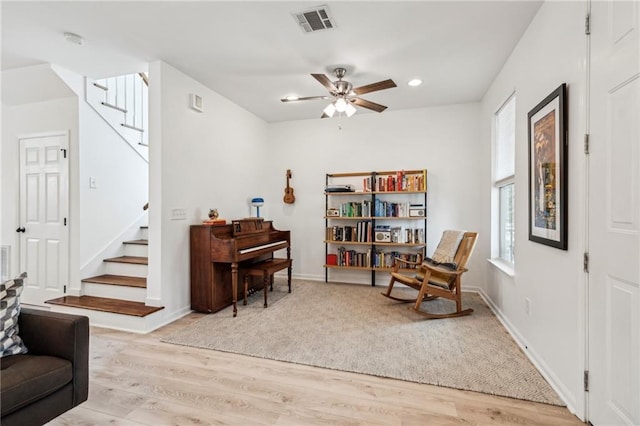 sitting room with stairs, light wood-style flooring, a ceiling fan, and visible vents