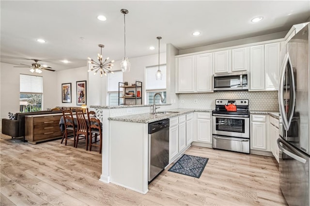 kitchen with light wood finished floors, backsplash, appliances with stainless steel finishes, a peninsula, and a sink