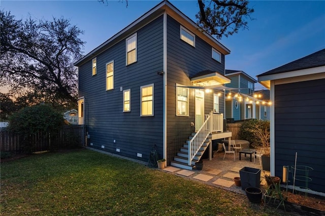 back of property at dusk featuring a patio, fence, a lawn, and crawl space