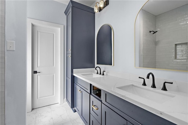 full bathroom with double vanity, marble finish floor, tiled shower, and a sink