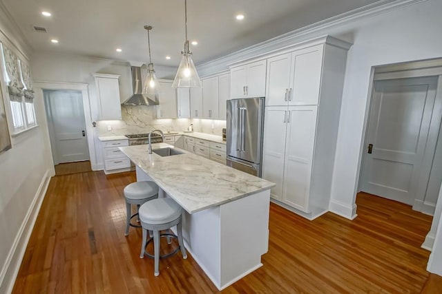 kitchen featuring visible vents, a kitchen island with sink, white cabinetry, high quality fridge, and wall chimney exhaust hood