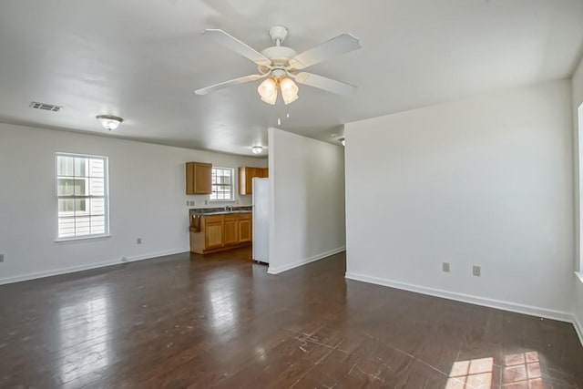 unfurnished living room with visible vents, baseboards, a sink, ceiling fan, and dark wood-type flooring