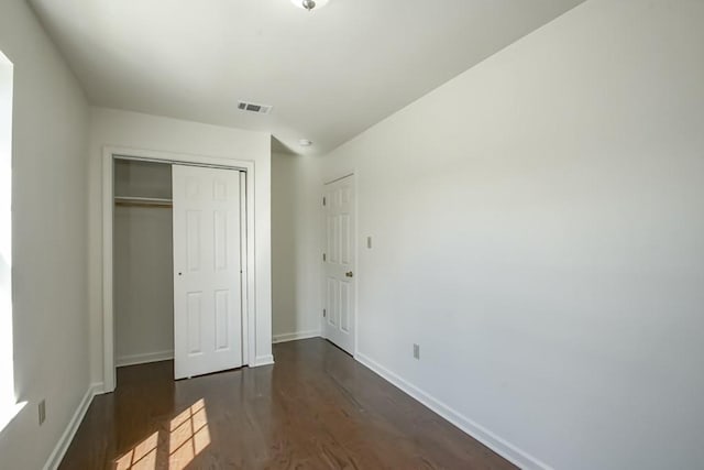 unfurnished bedroom with dark wood-type flooring, baseboards, visible vents, and a closet