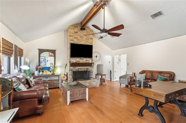 living area with visible vents, ceiling fan, beamed ceiling, a fireplace, and wood finished floors