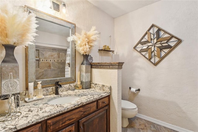 full bathroom with vanity, toilet, a textured wall, and baseboards