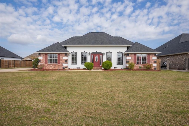 view of front of home with stucco siding, a front lawn, fence, a shingled roof, and brick siding