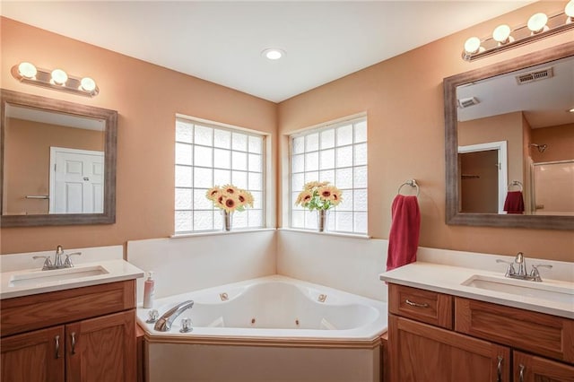 full bath with two vanities, a tub with jets, visible vents, and a sink