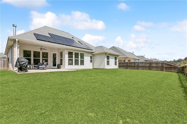 rear view of house featuring a patio, a ceiling fan, solar panels, a yard, and a fenced backyard